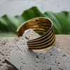Gold and black striped bracelet on a textured stone surface with green leaves in the background