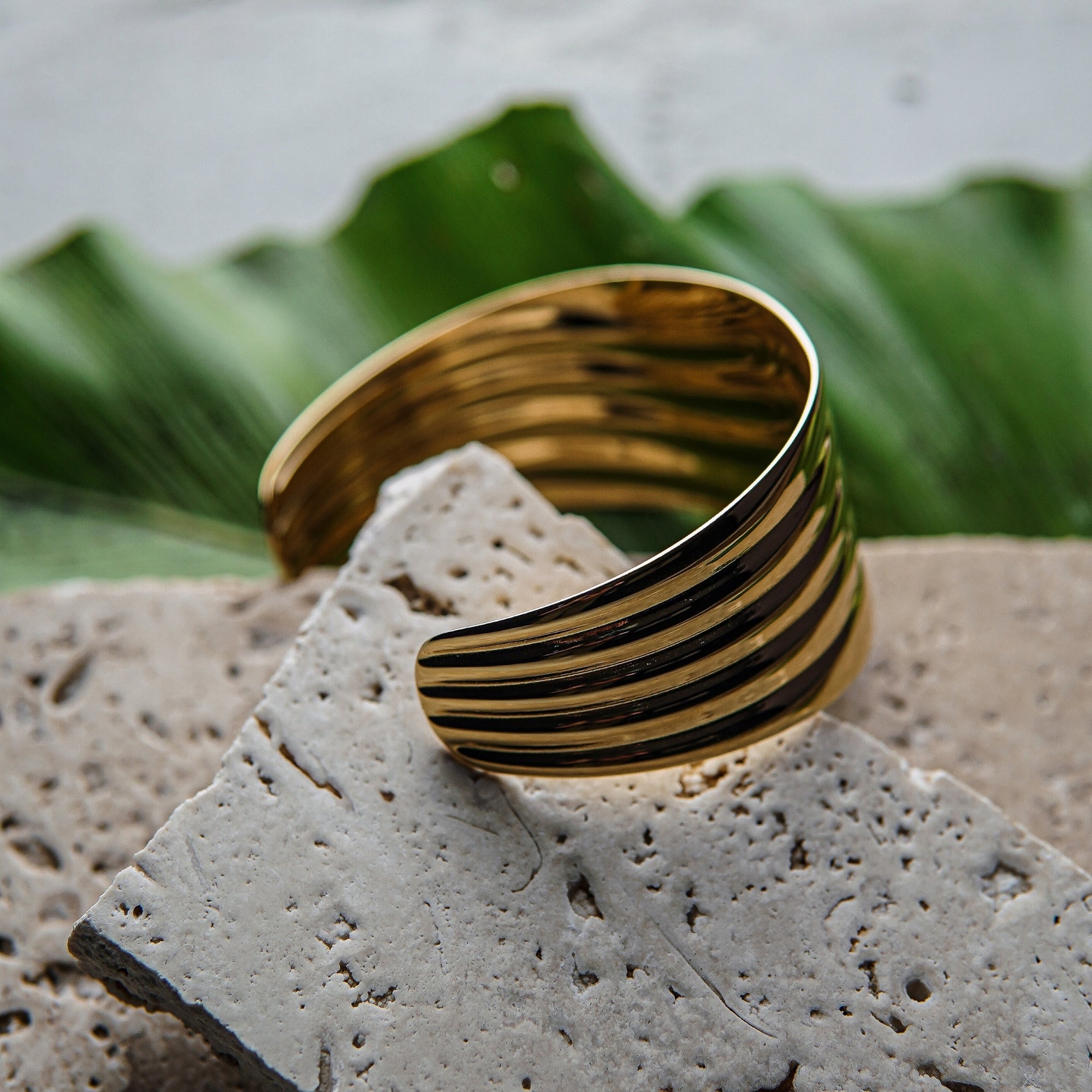 Gold and black striped bracelet on a textured stone surface with green leaves in the background