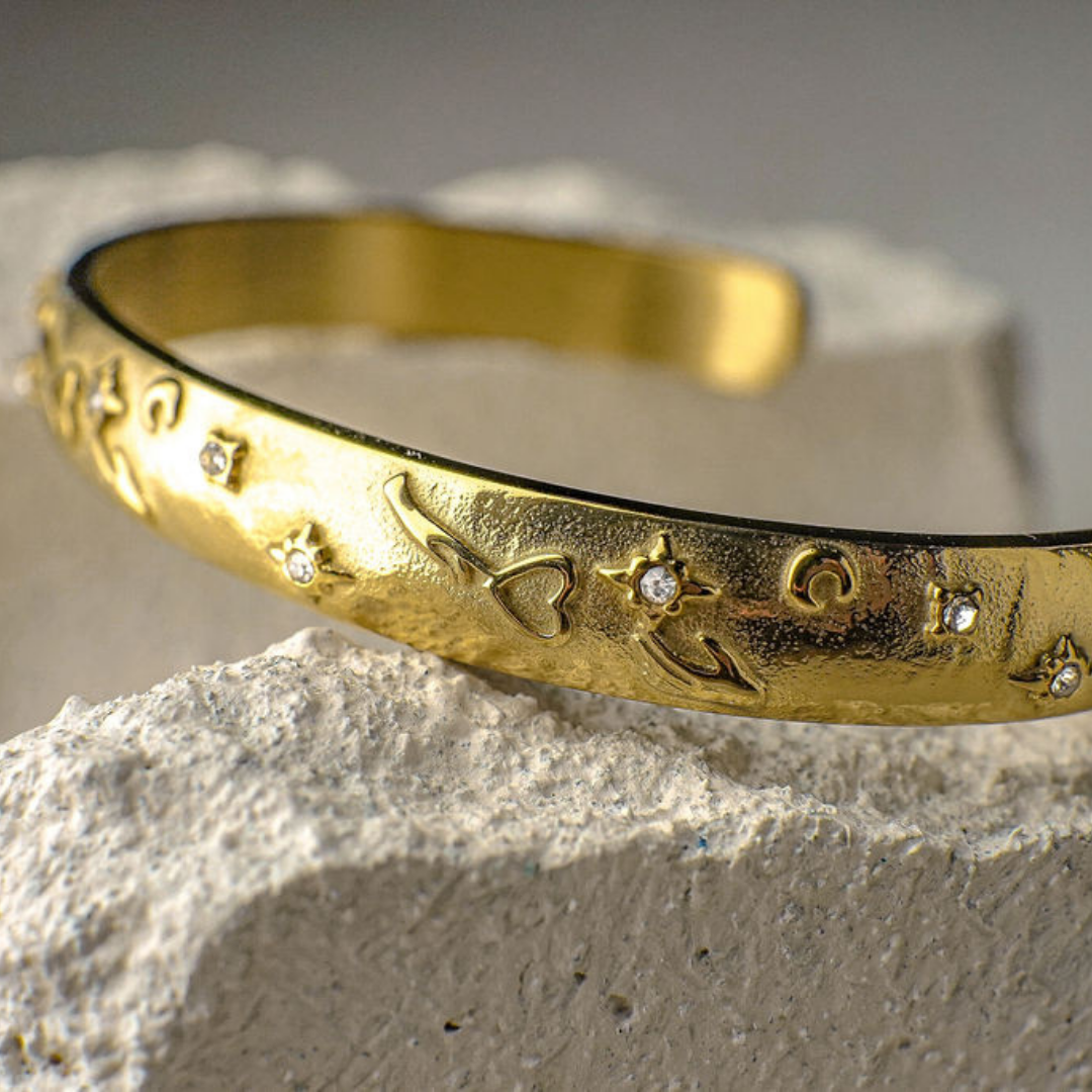 Gold bracelet with engraved designs on a textured surface