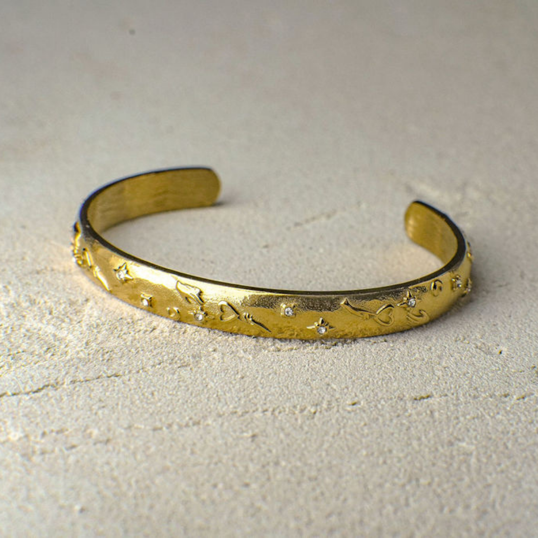 Gold bracelet with engraved designs on a light gray background