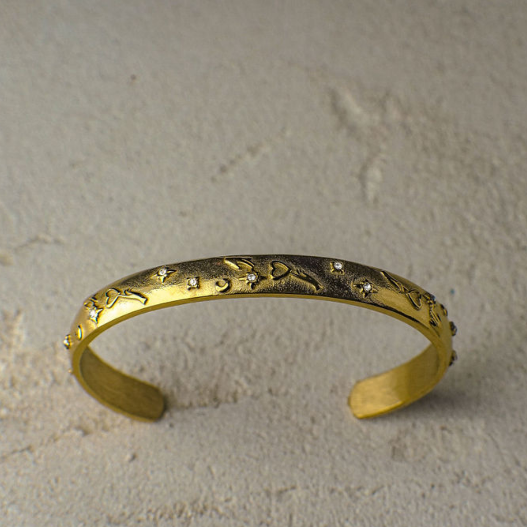 A gold bangle bracelet with engraving and little crystals on a textured surface