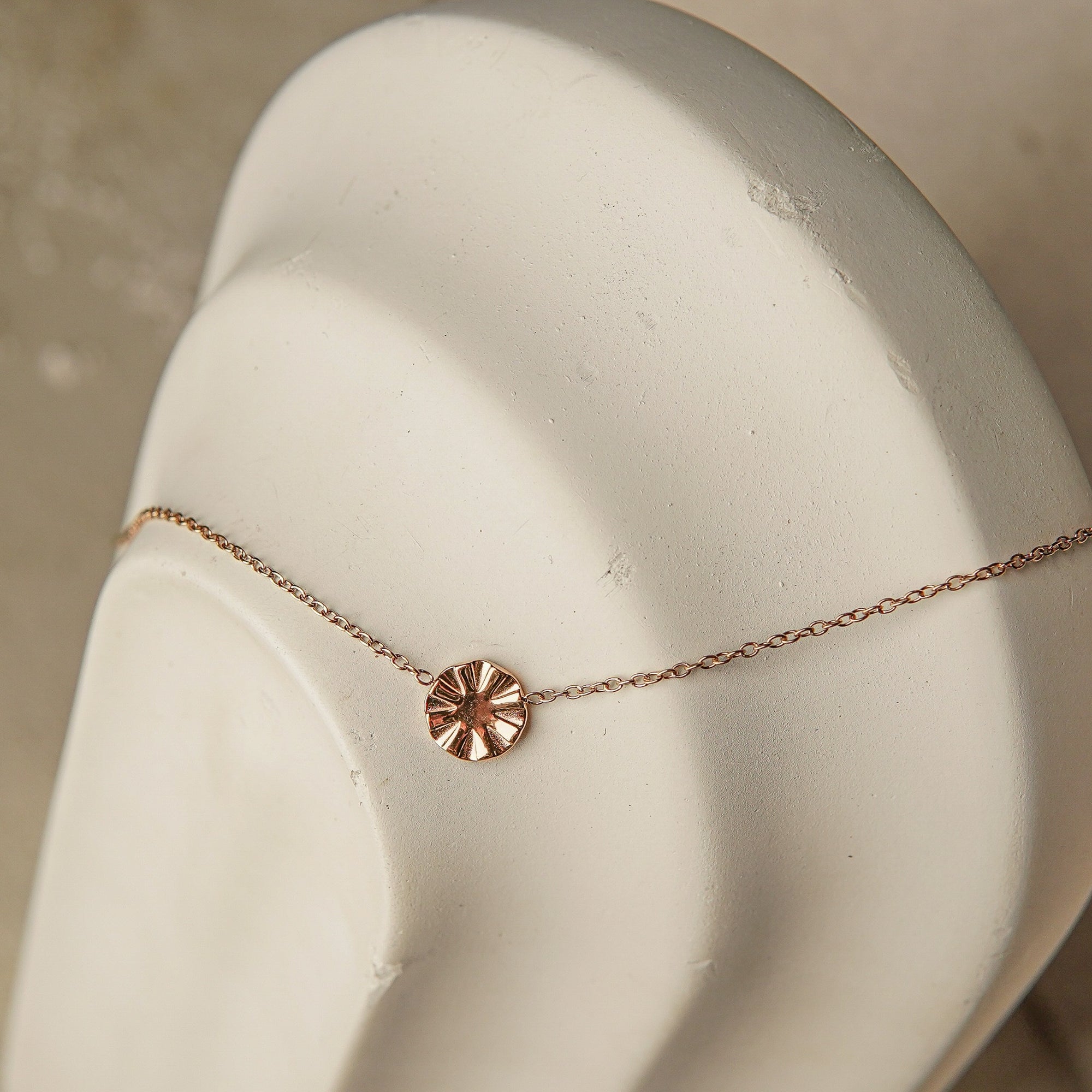 Rose gold necklace with a circular pendant on a mannequin bust.