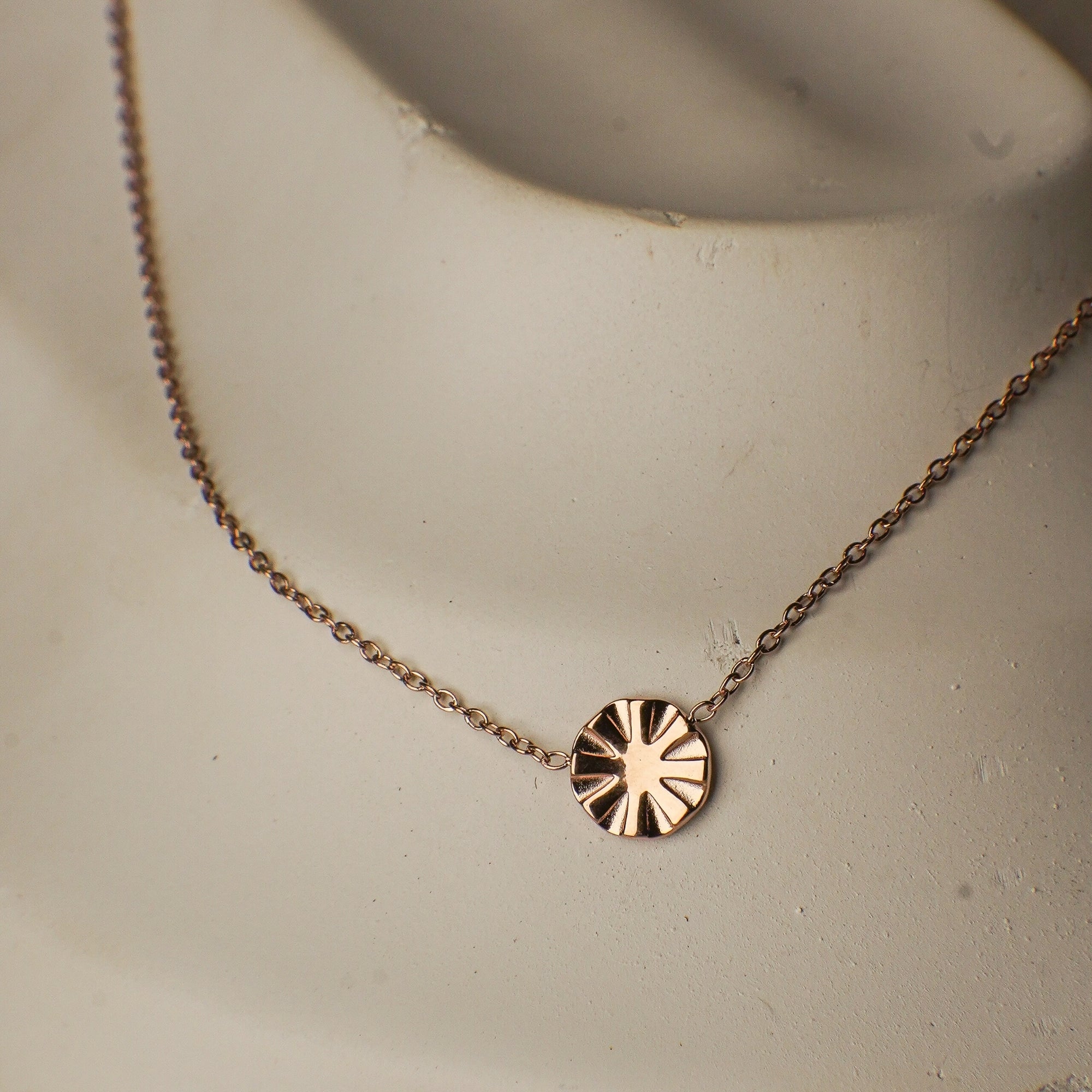 Rose gold necklace with a circular pendant on a neutral background