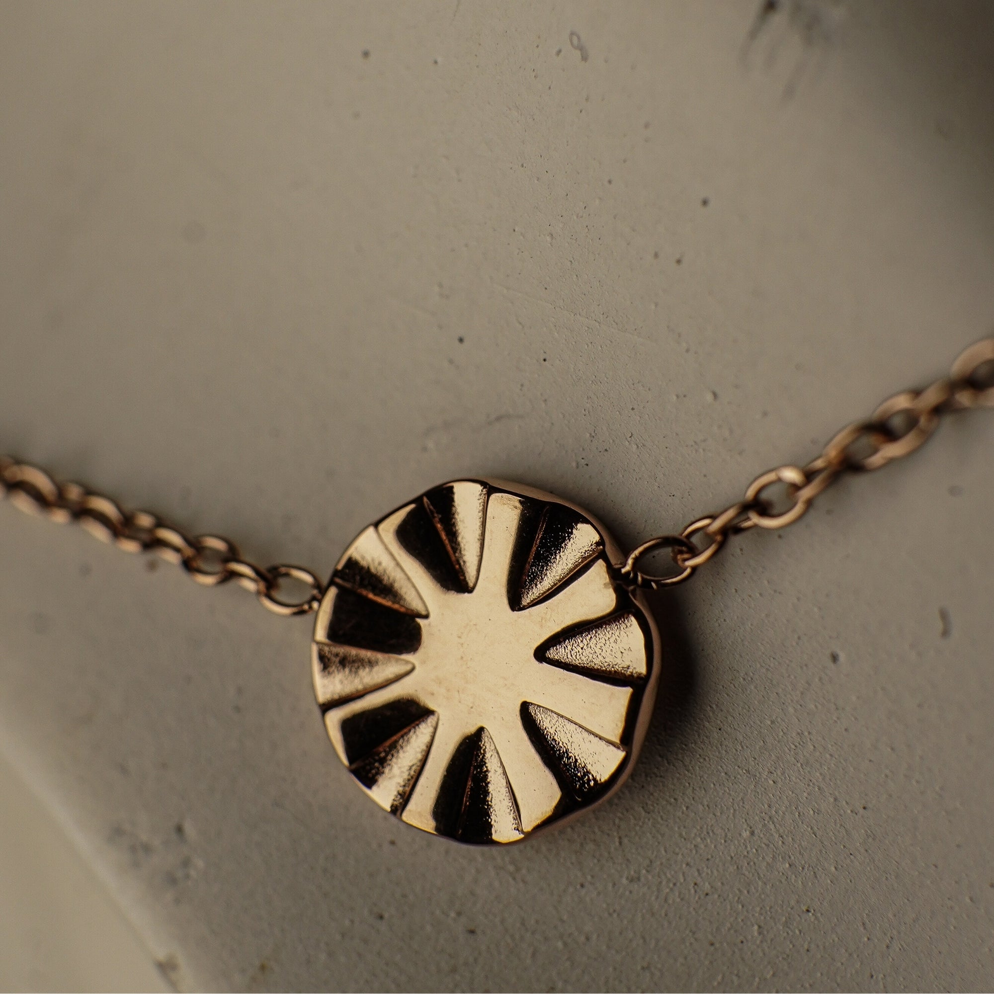 Rose gold necklace with a sun-shaped pendant on a neutral background