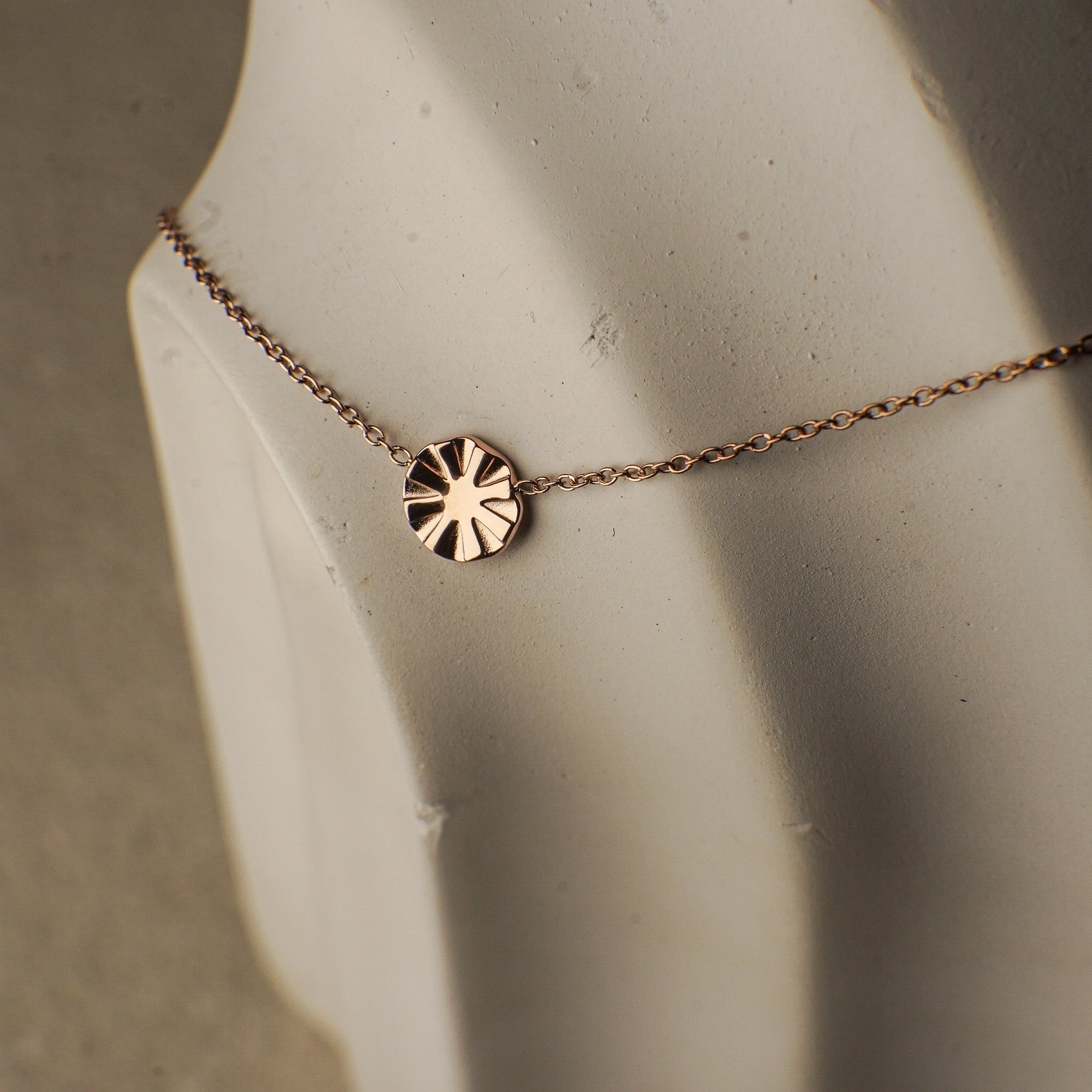 Rose gold necklace with a round pendant on a mannequin bust.