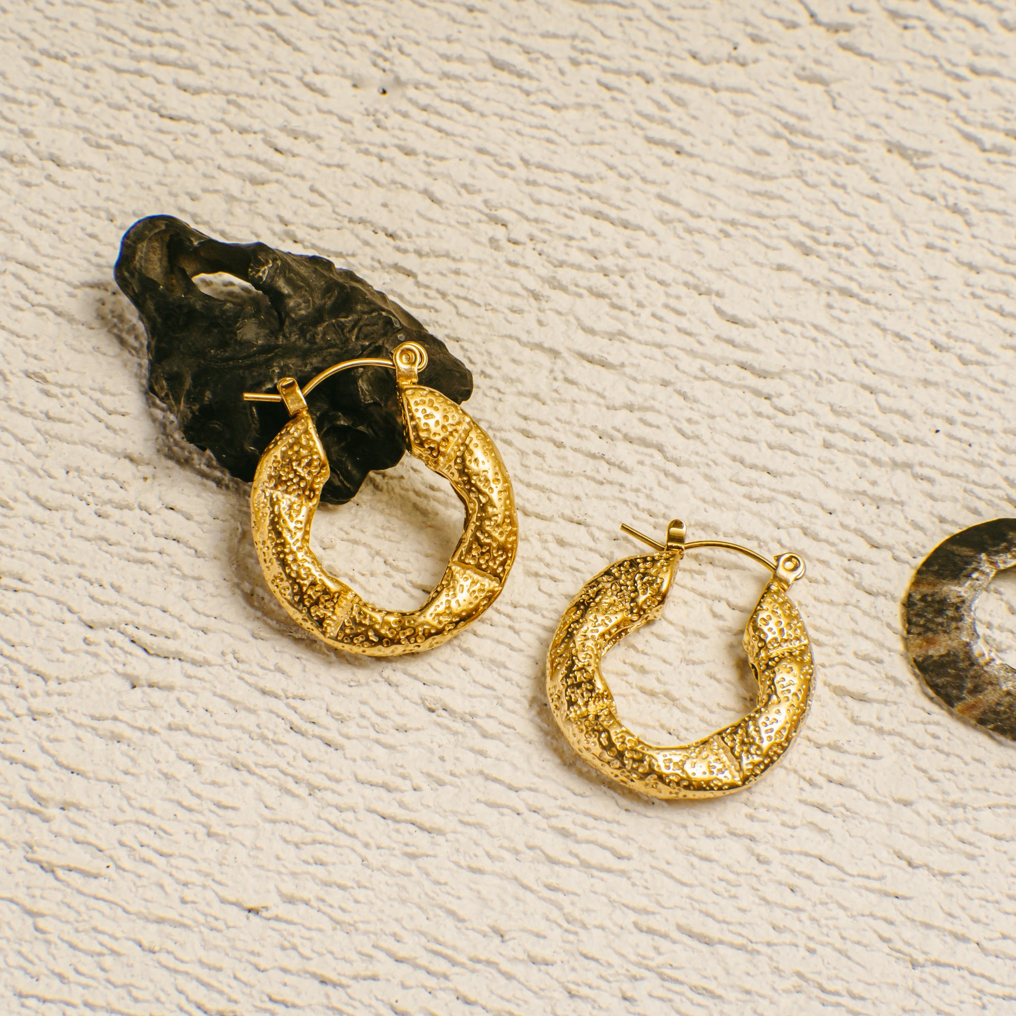 Gold hoop earrings on a textured beige surface