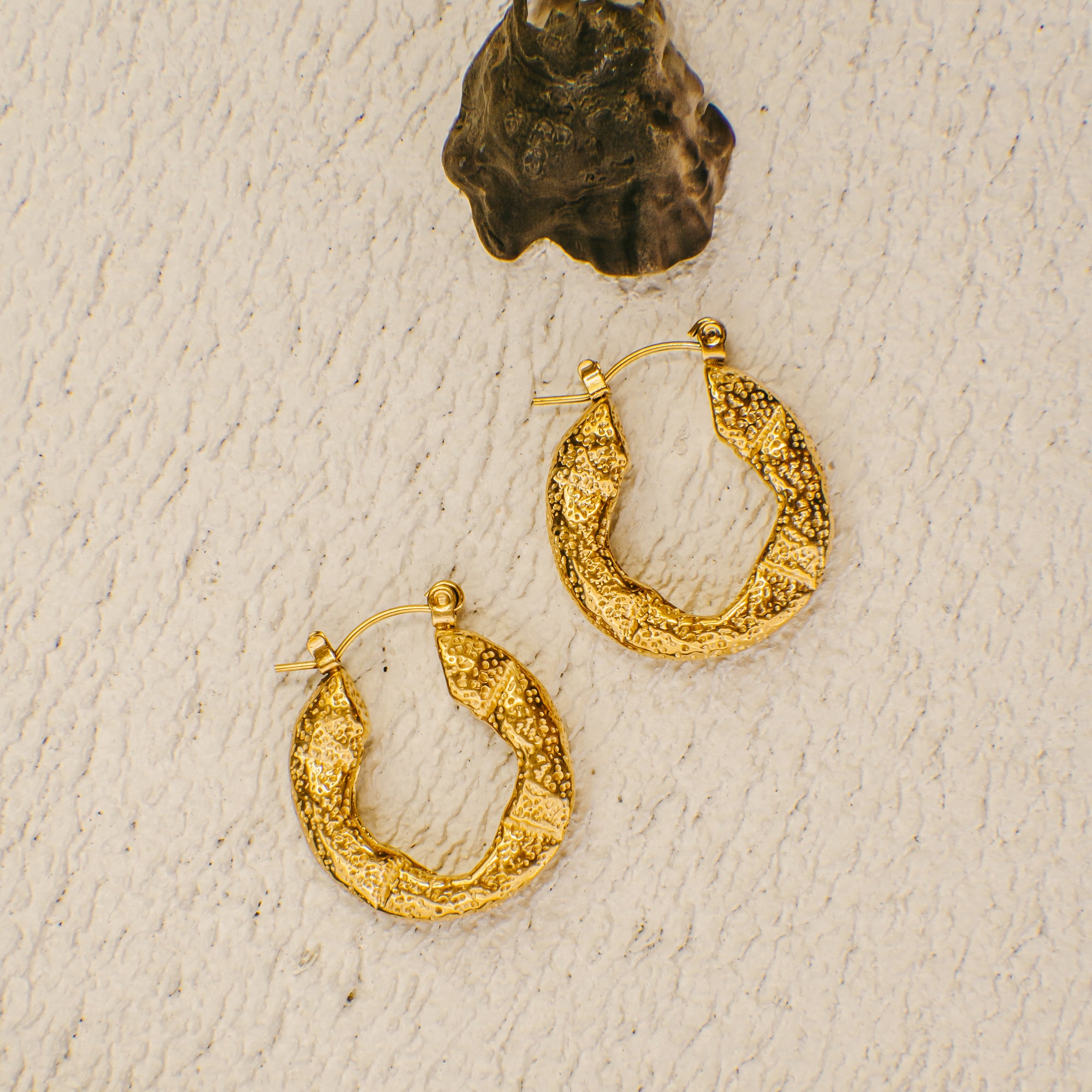 Gold hoop earrings on a textured beige surface
