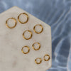 A collection of gold earrings with different sizes on a beige stuface
