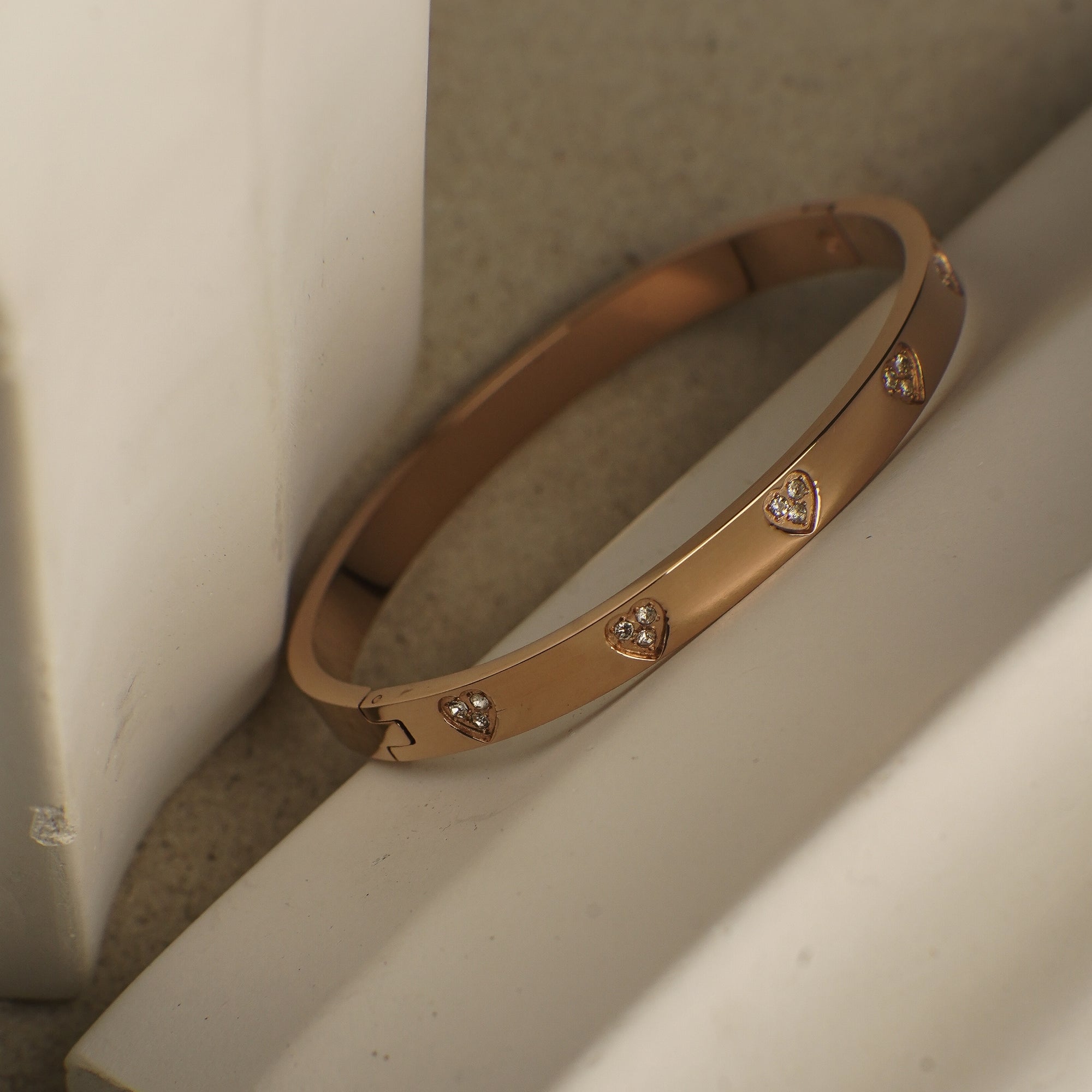 Rose gold bracelet with heart-shaped diamond accents on a light background