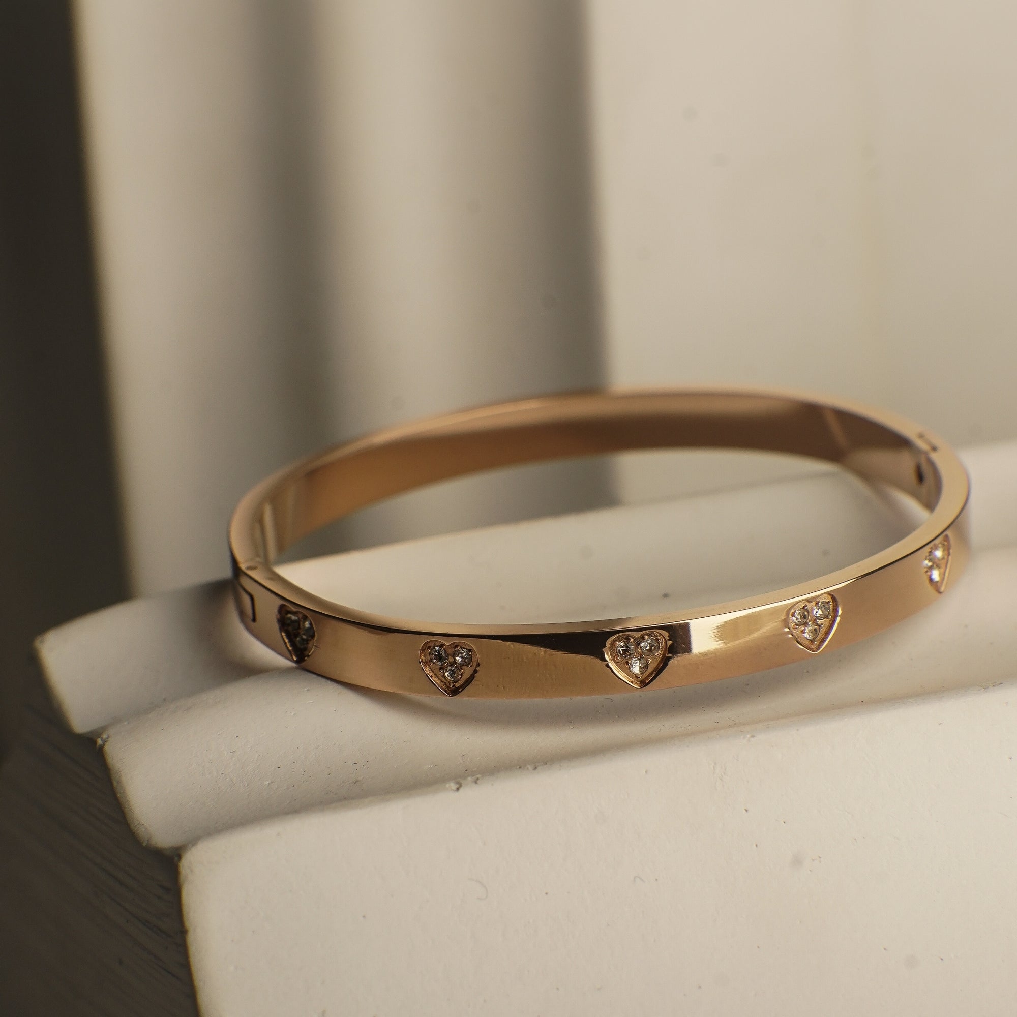 Gold bracelet with heart-shaped diamond accents on a white stand.