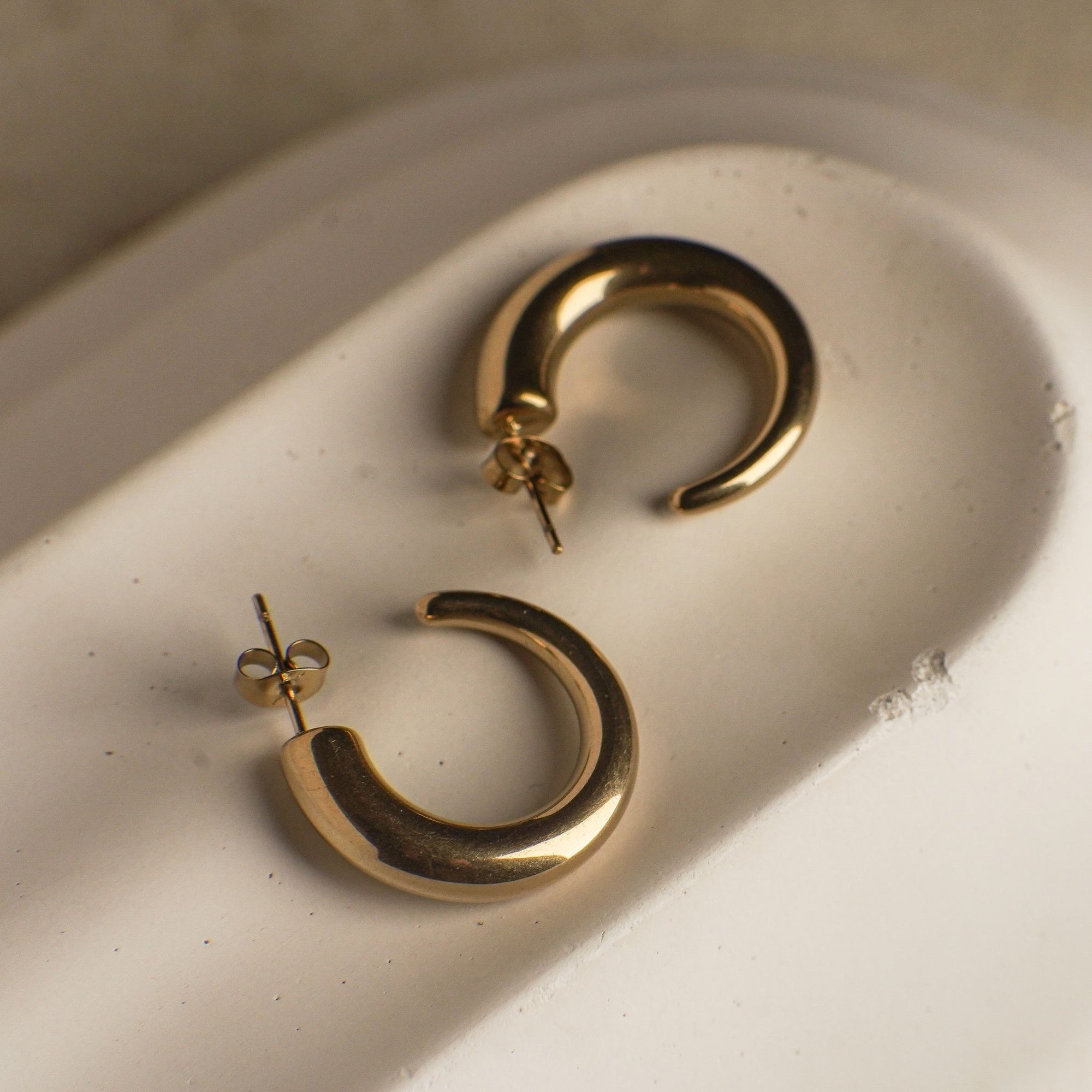 Gold hoop earrings on a textured beige surface