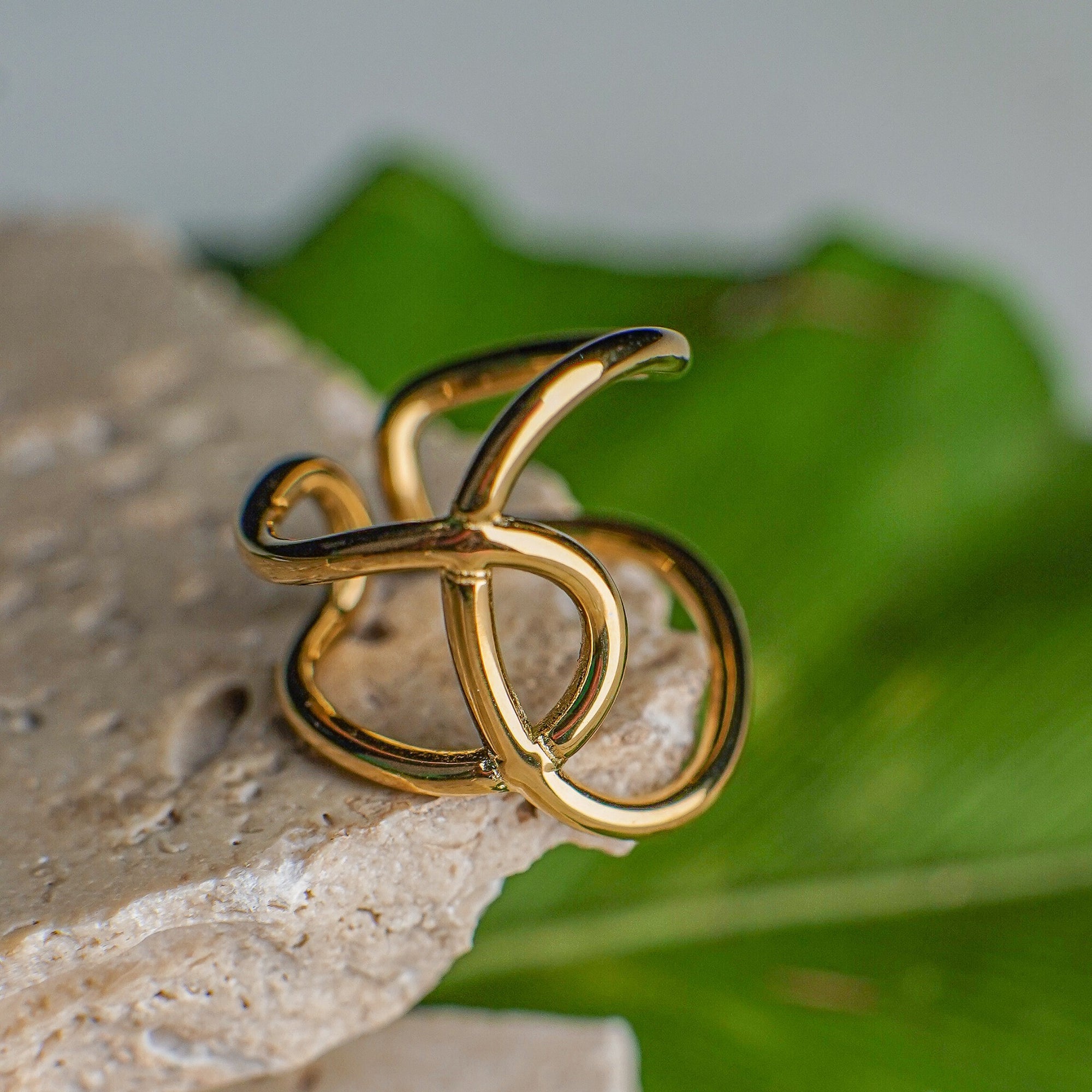 Gold ring with a unique design on a stone surface with green leaves in the background