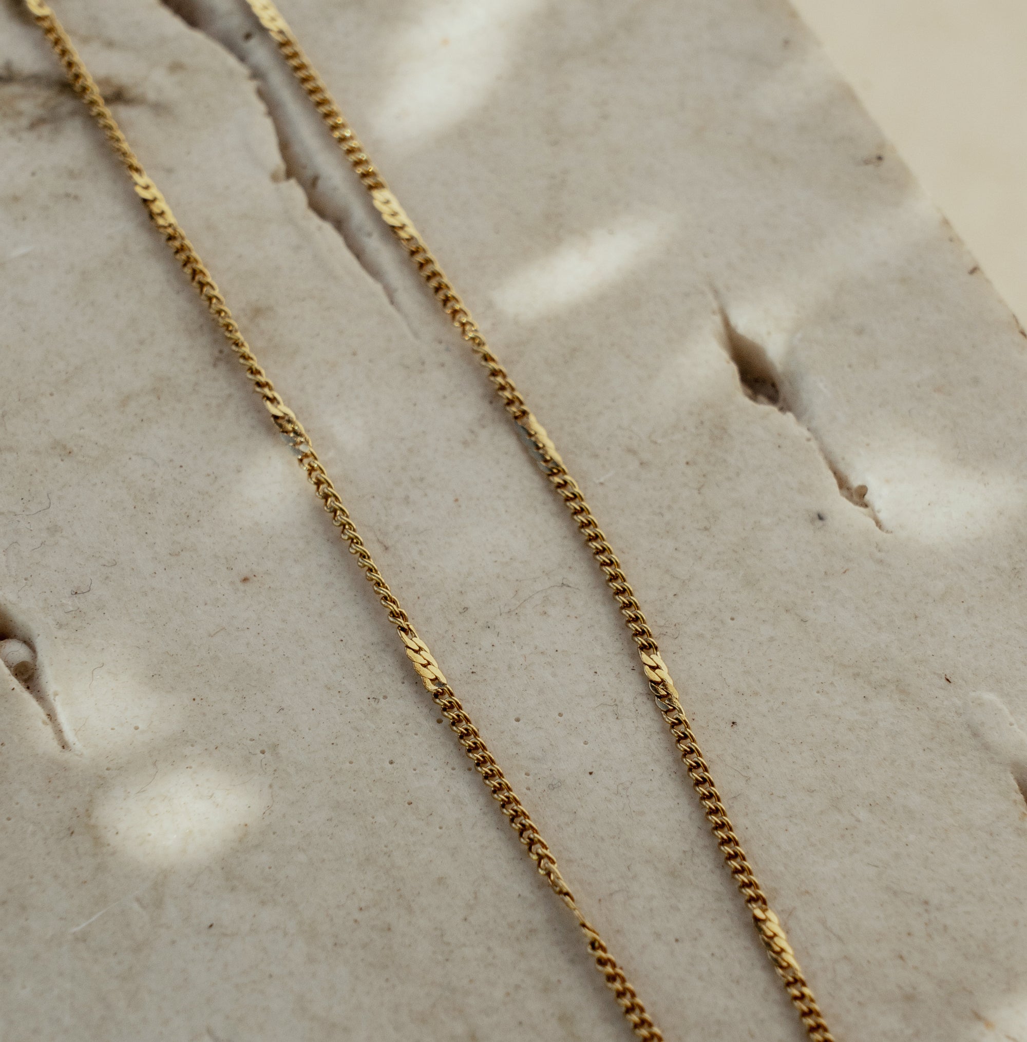 A gold-colored necklace laid out on a textured surface.