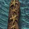 Gold starfish decorations on a piece of driftwood with water in the background