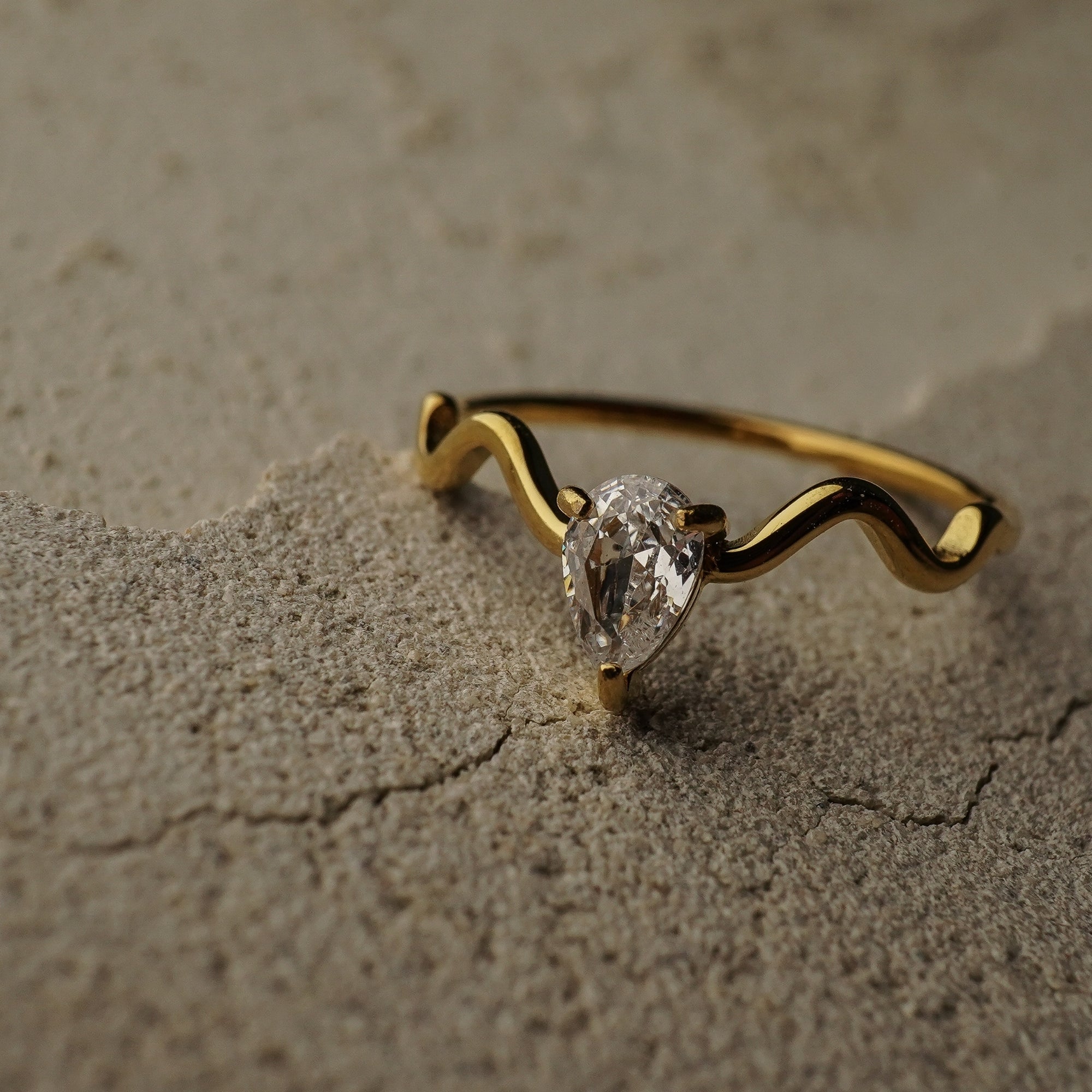 Gold ring with a diamond on a textured beige surface