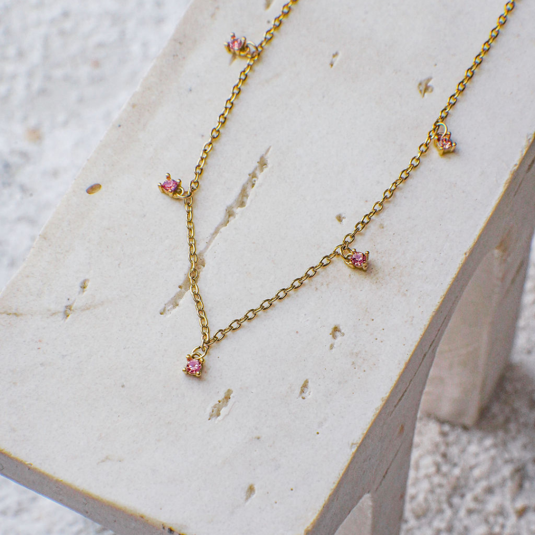 Gold necklace with pink gemstones on a marble surface