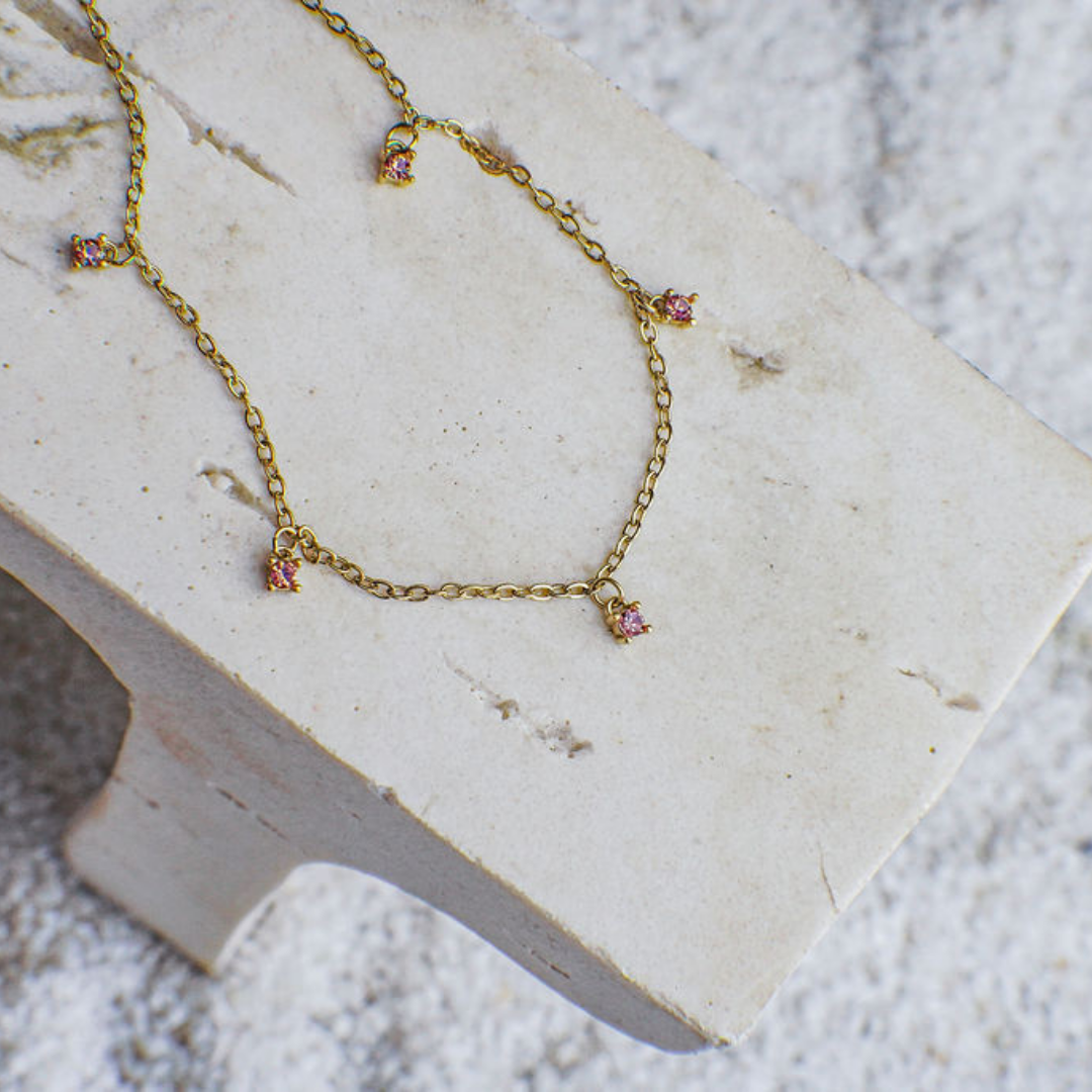 Gold necklace with pink gemstones on a white stone surface