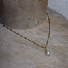 Gold chain necklace with a pearl pendant on a textured surface
