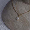 Gold necklace with a pearl pendant on a textured stone surface