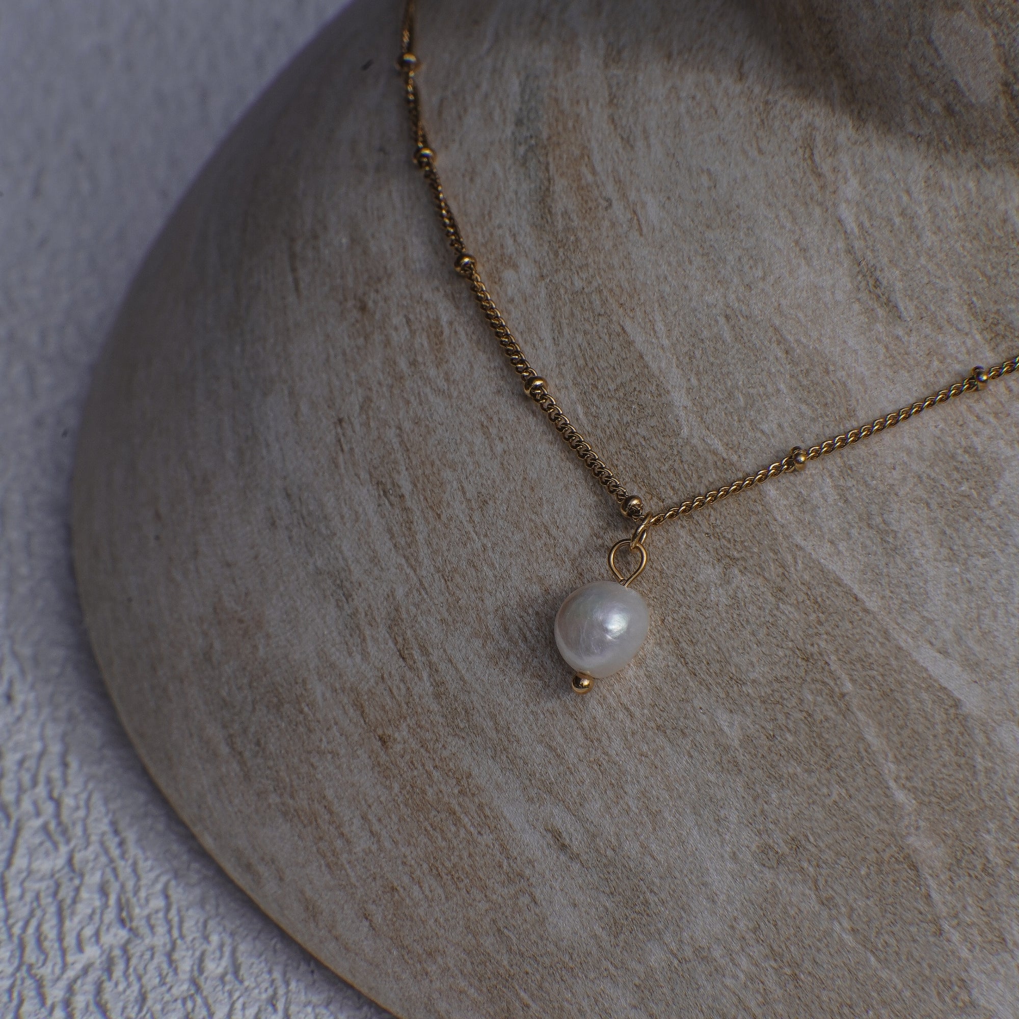 Gold necklace with a pearl pendant on a textured stone surface
