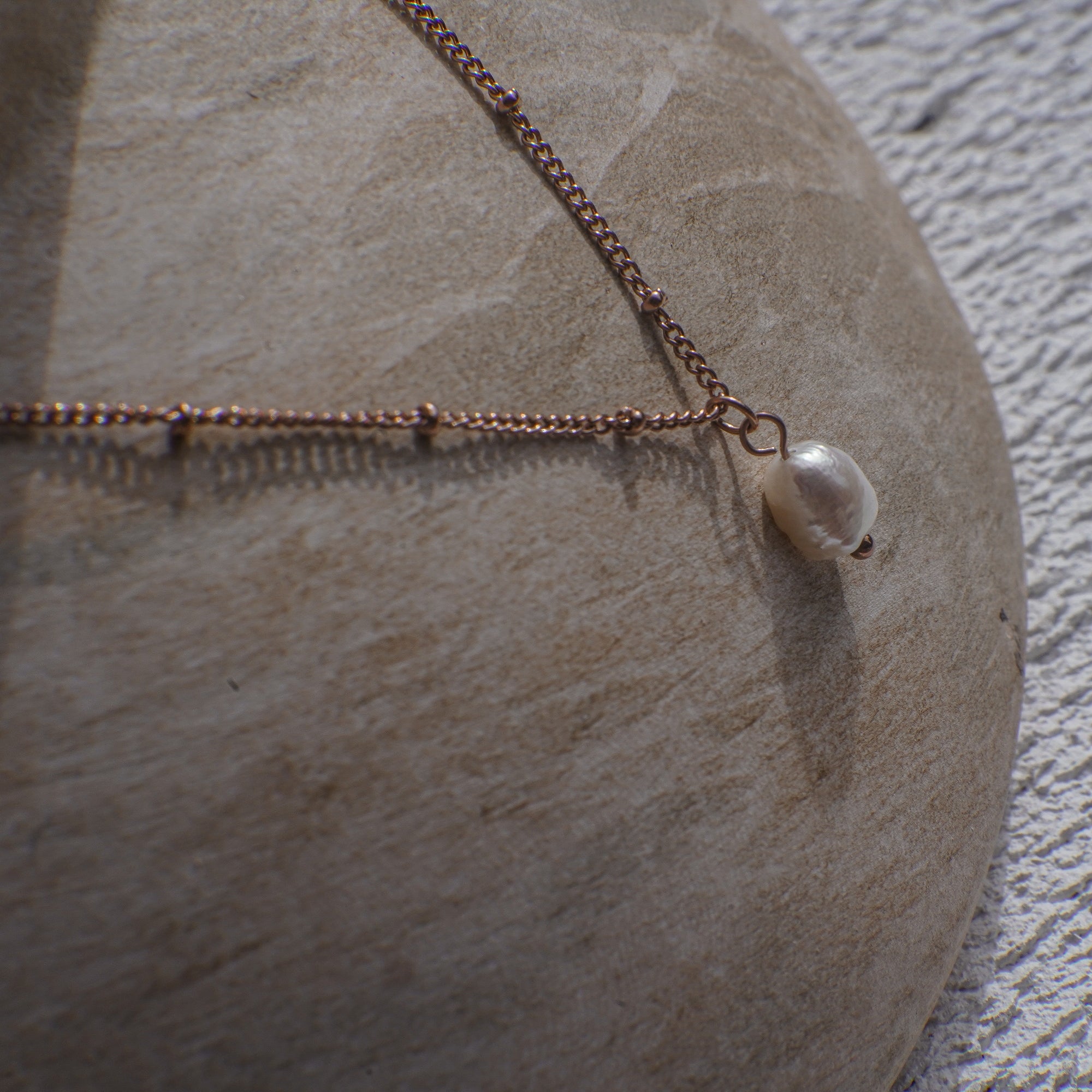 Necklace with a pearl pendant on a stone surface