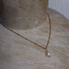Gold chain necklace with a pearl pendant on a textured surface