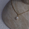 Gold necklace with a pearl pendant on a textured stone surface