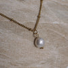 Gold chain necklace with a pearl pendant on a stone surface