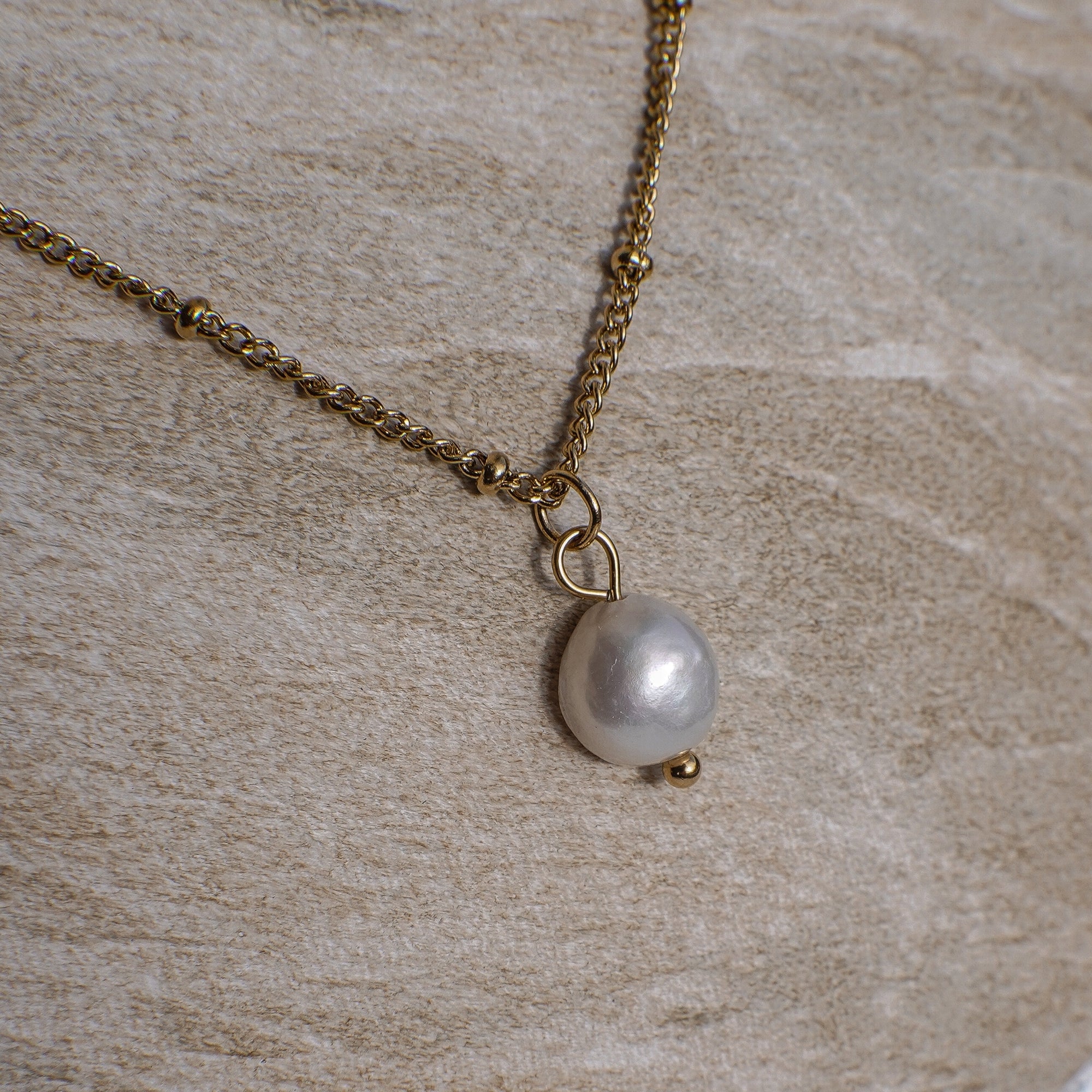 Gold chain necklace with a pearl pendant on a stone surface
