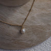 Gold necklace with a single pearl pendant on a stone surface