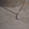 Necklace with a pearl pendant on a beige stone surface