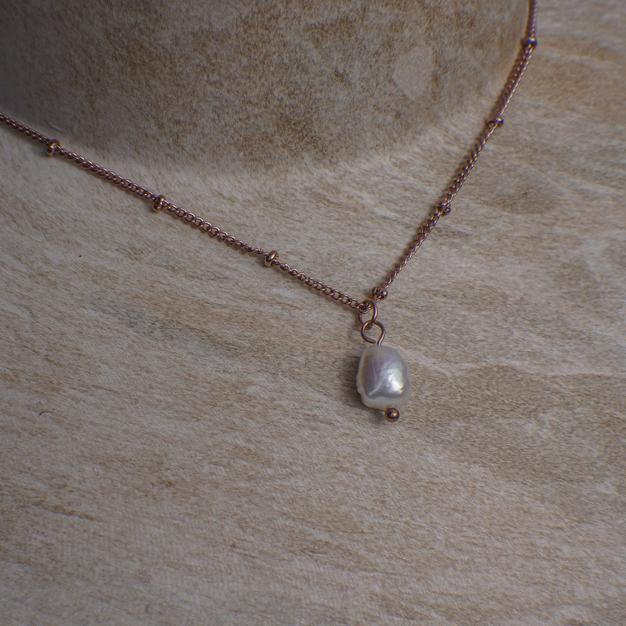 Necklace with a pearl pendant on a beige stone surface