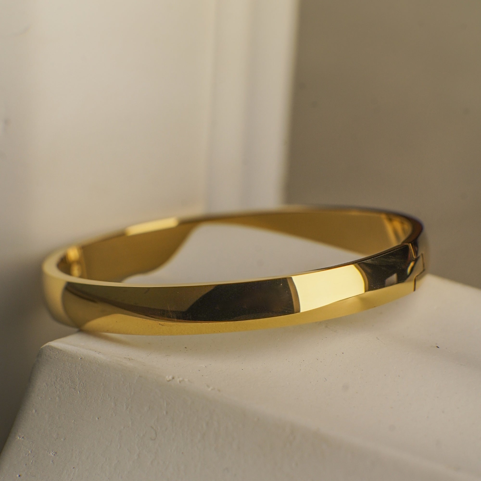 Gold bracelet on a white pedestal with a neutral background