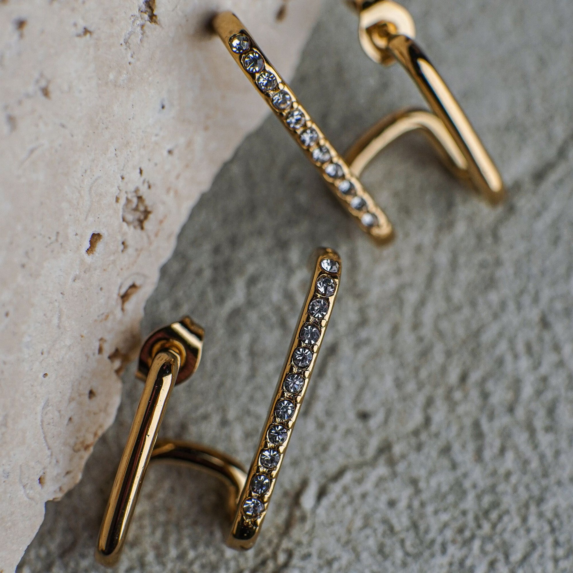 Gold earrings with gemstones on a textured surface