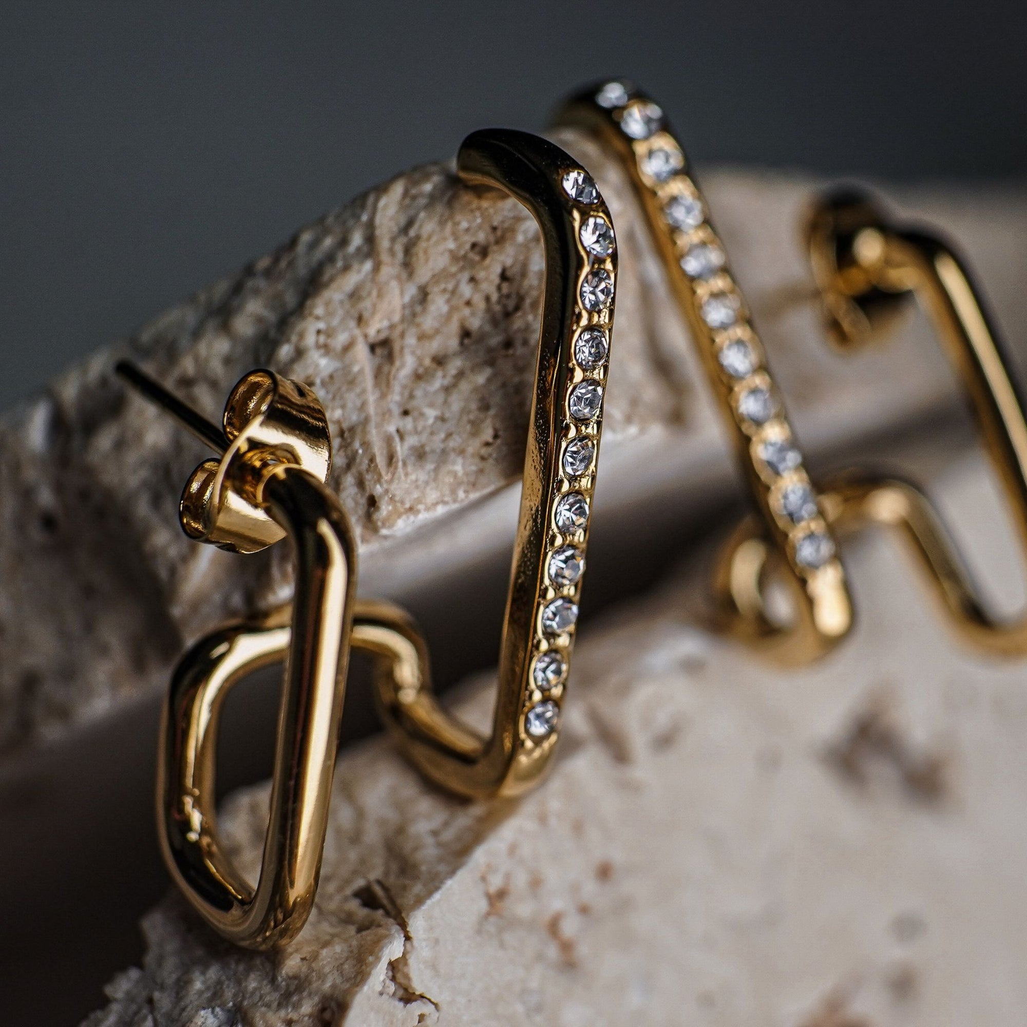 Gold hoop earrings with embedded stones on a stone surface