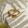 A gold ring with clear zirconia stones set around its circumference, placed on a textured surface with a blurred background.