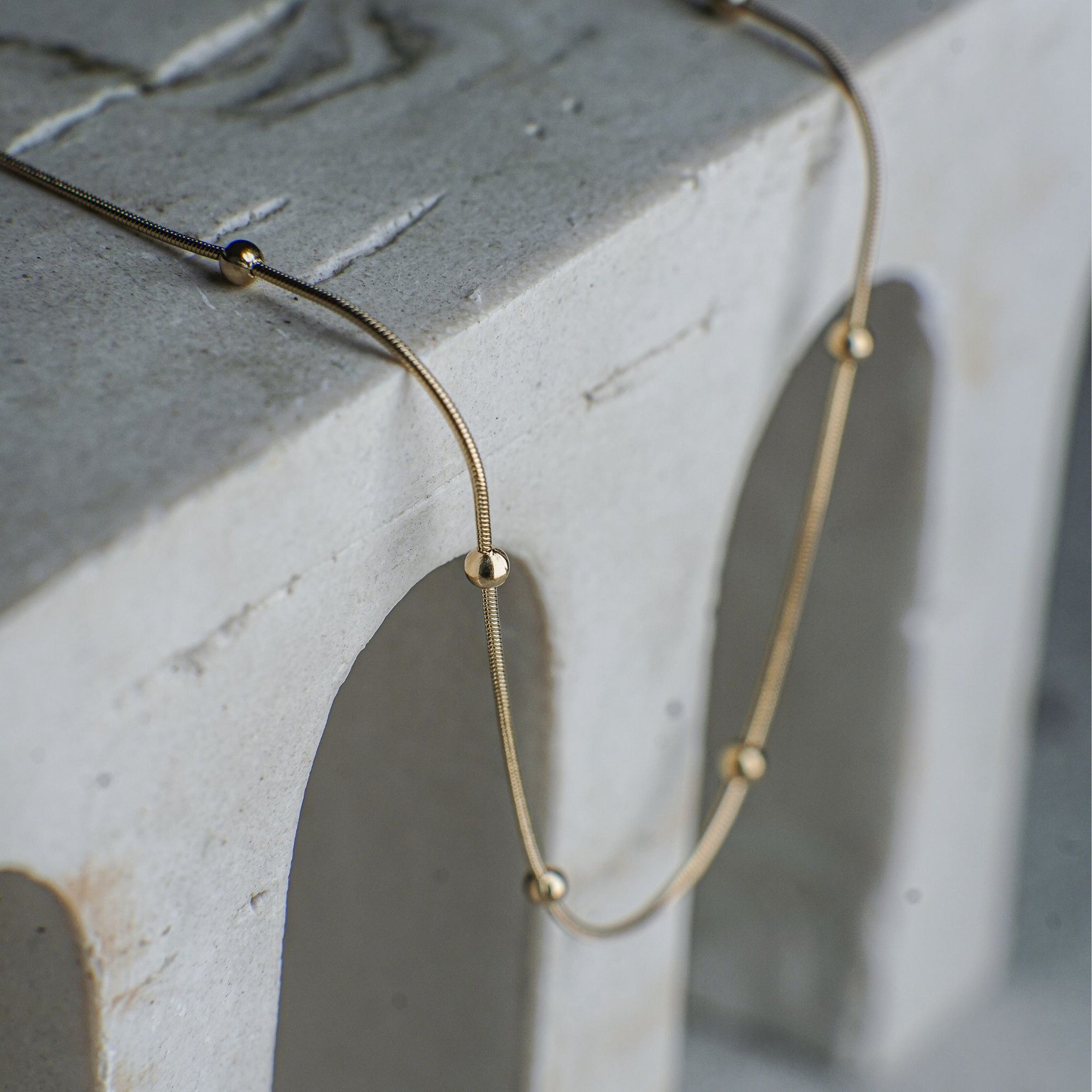 Gold necklace with small beads on a concrete surface