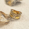 Gold ring with gemstones on a textured beige surface