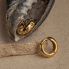 A pair of gold huggie earrings with small cubic zirconia embellishments, displayed on a textured surface.