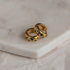 A pair of gold-colored huggie earrings with emerald zirconia stones on a marble surface.