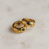 A pair of gold-colored multi-colored zirconia huggie earrings on a marble surface.