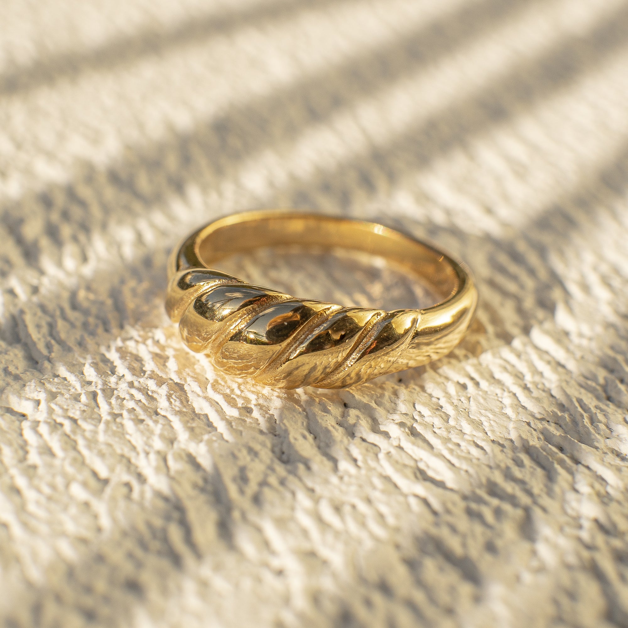 A gold ribbed dome ring on a textured surface