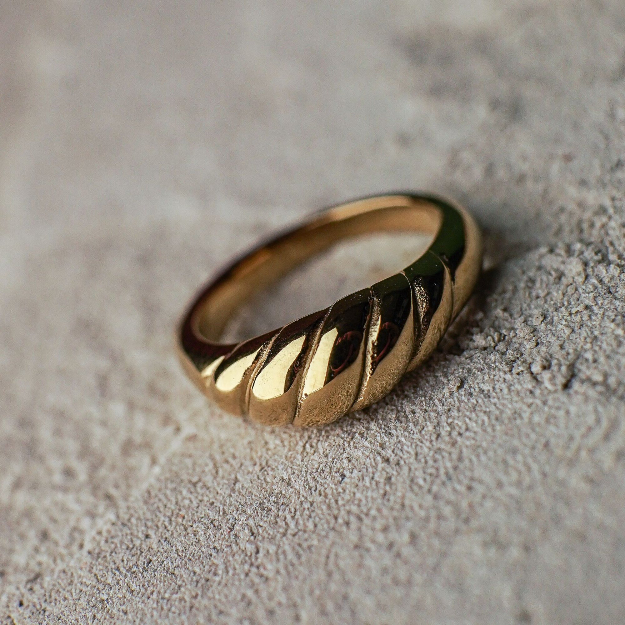 Gold ring with a textured band on a sandy surface
