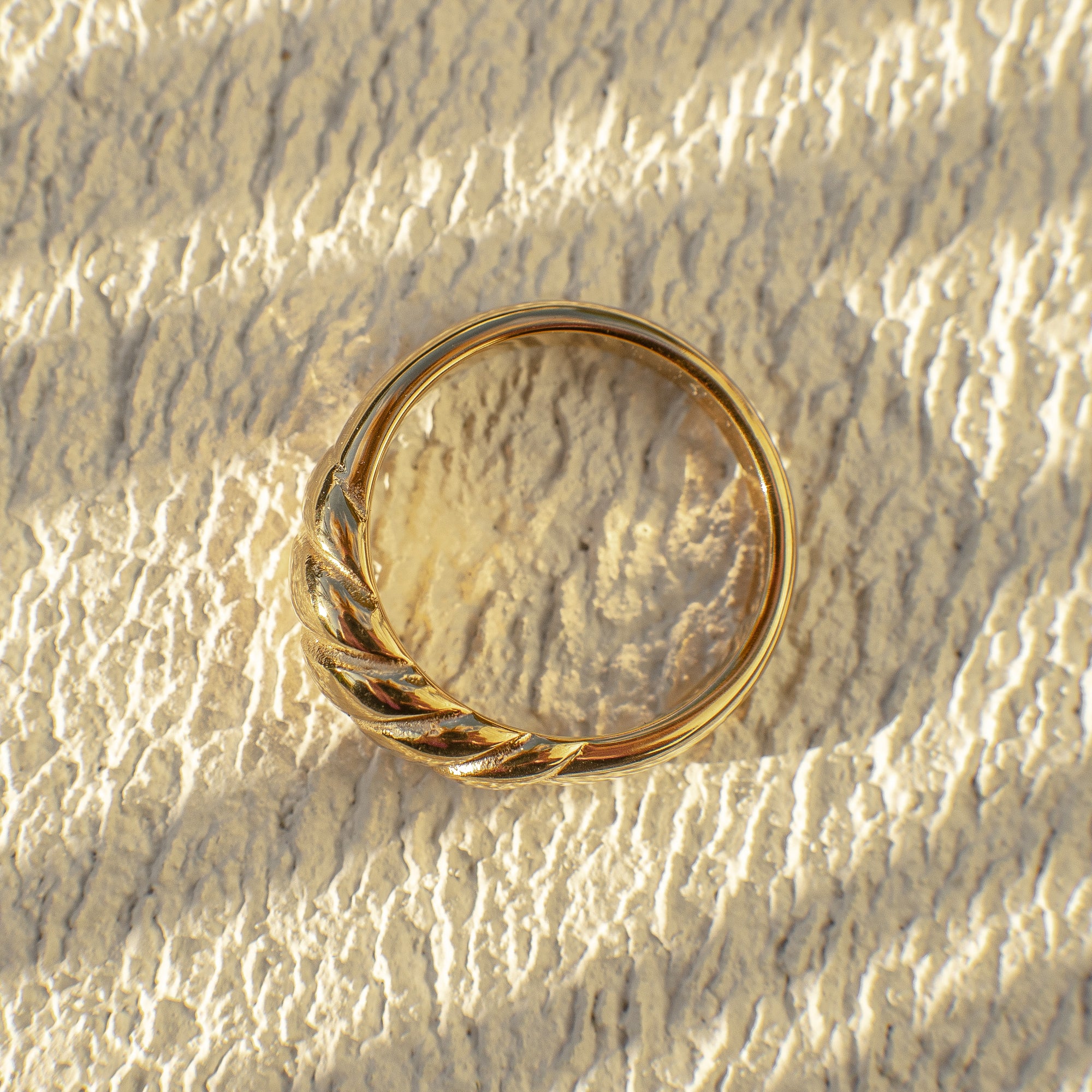A gold ribbed dome ring on a textured surface