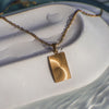 Gold necklace with a rectangular pendant on a textured white surface