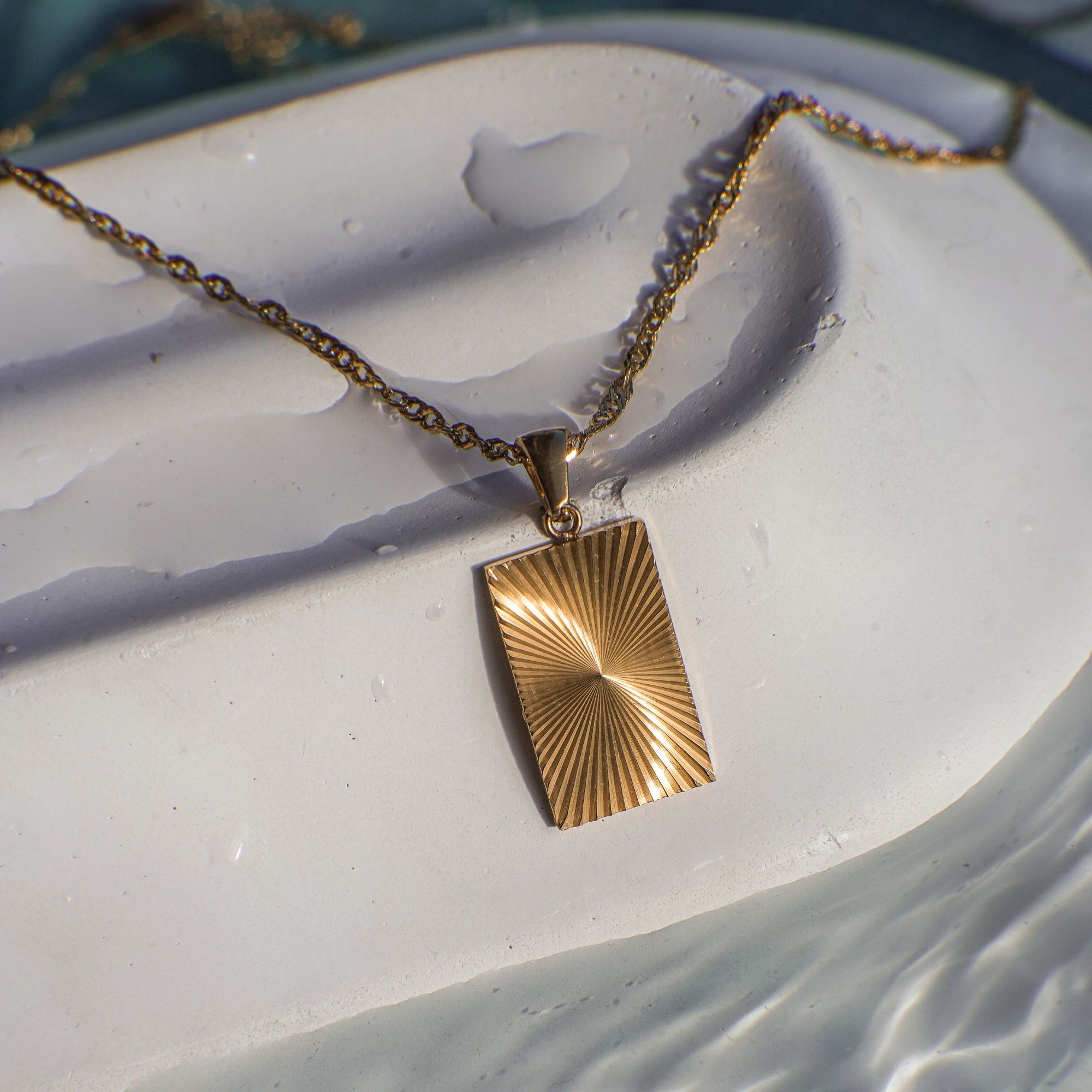 Gold necklace with a rectangular pendant on a textured white surface