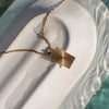 Gold necklace with a geometric pendant on a textured white surface