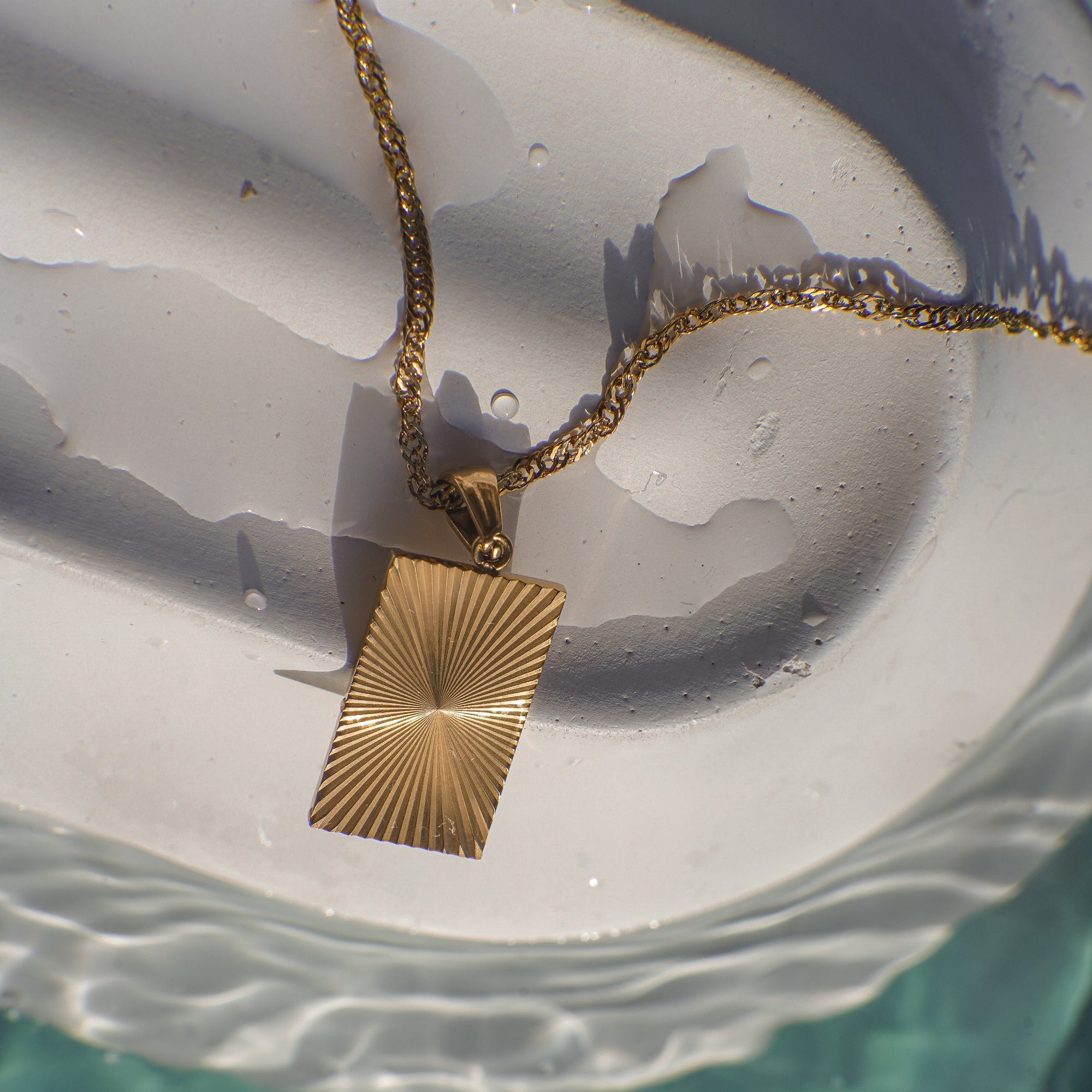 Gold necklace with a textured pendant on a white shell