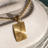 Gold necklace with a textured pendant on a textured white surface