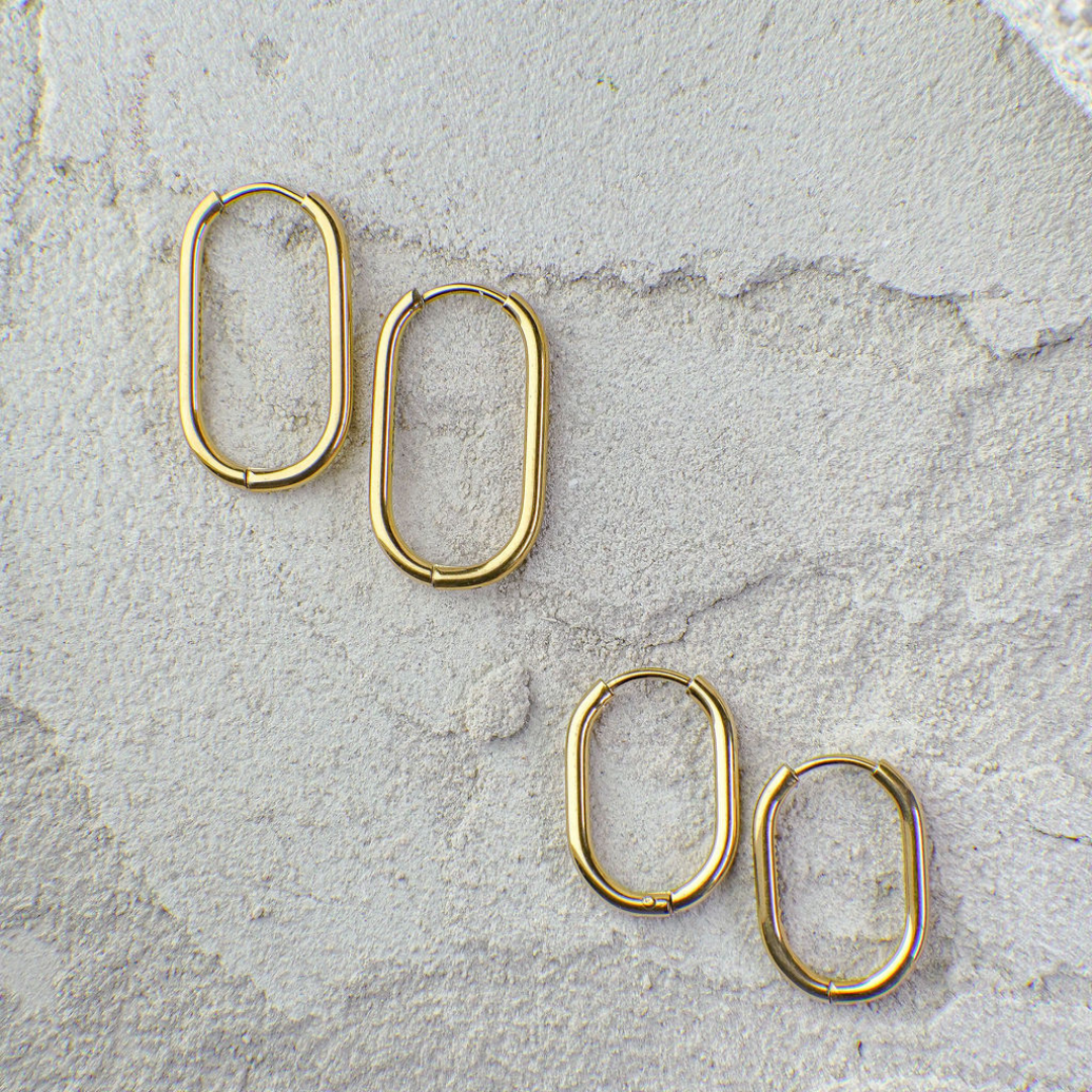 Set of gold hoop earrings on a textured stone surface